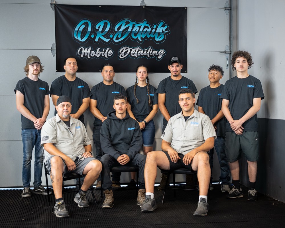 The O.R. Details mobile detailing crew posed under their shop banner